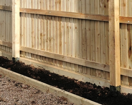 A newly built fence with plastic sleeves around the base of the structural posts.