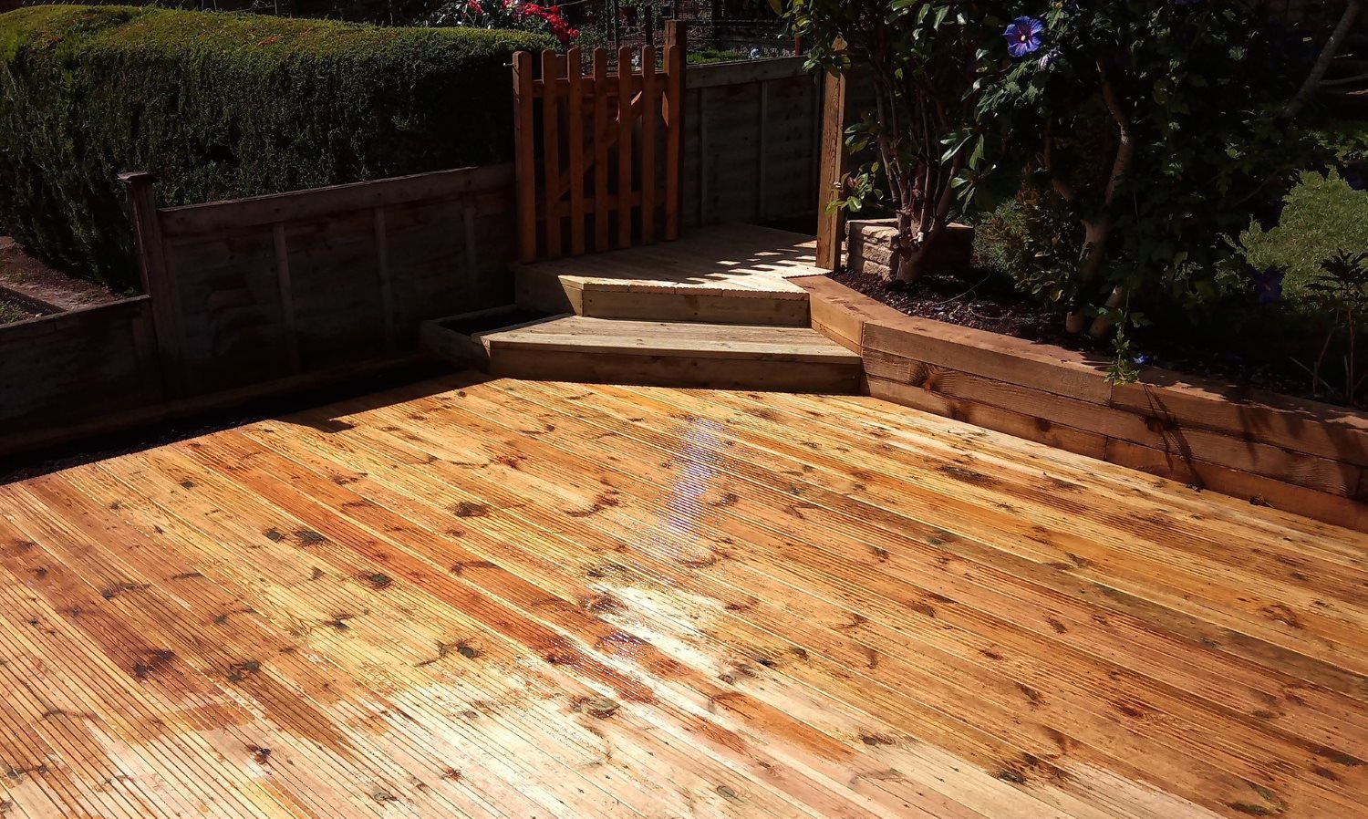 New decking area created with bespoke flush flower beds along the fence and wooden steps in the corner to a gate.