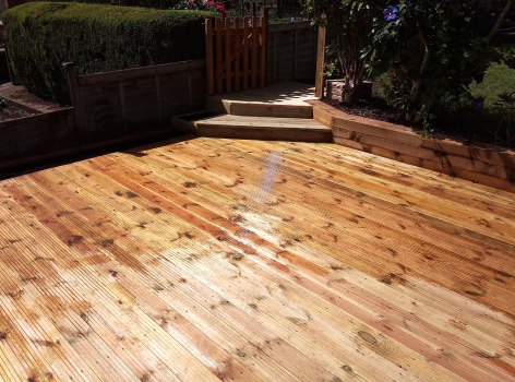 New decking area created with bespoke flush flower beds along the fence and wooden steps in the corner to a gate.