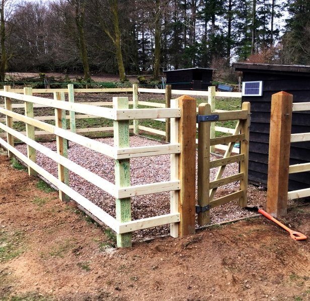A field with an enclosed area for an electrical utilities shed constructed with post and rail fencing and a wooden pedestrian gate.