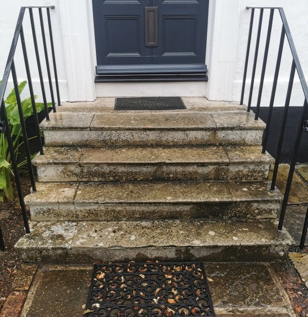Natural stone stairs leading to a front door of a Georgian house are stained in black with white lichen growth before a clean.